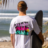 Fun Day Surf Aloha Tee in White back graphic worn with a surfboard at the beach, lifestyle view