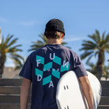 Fun Day Surf Checks Tee in Navy back graphic next to a surfboard, lifestyle view