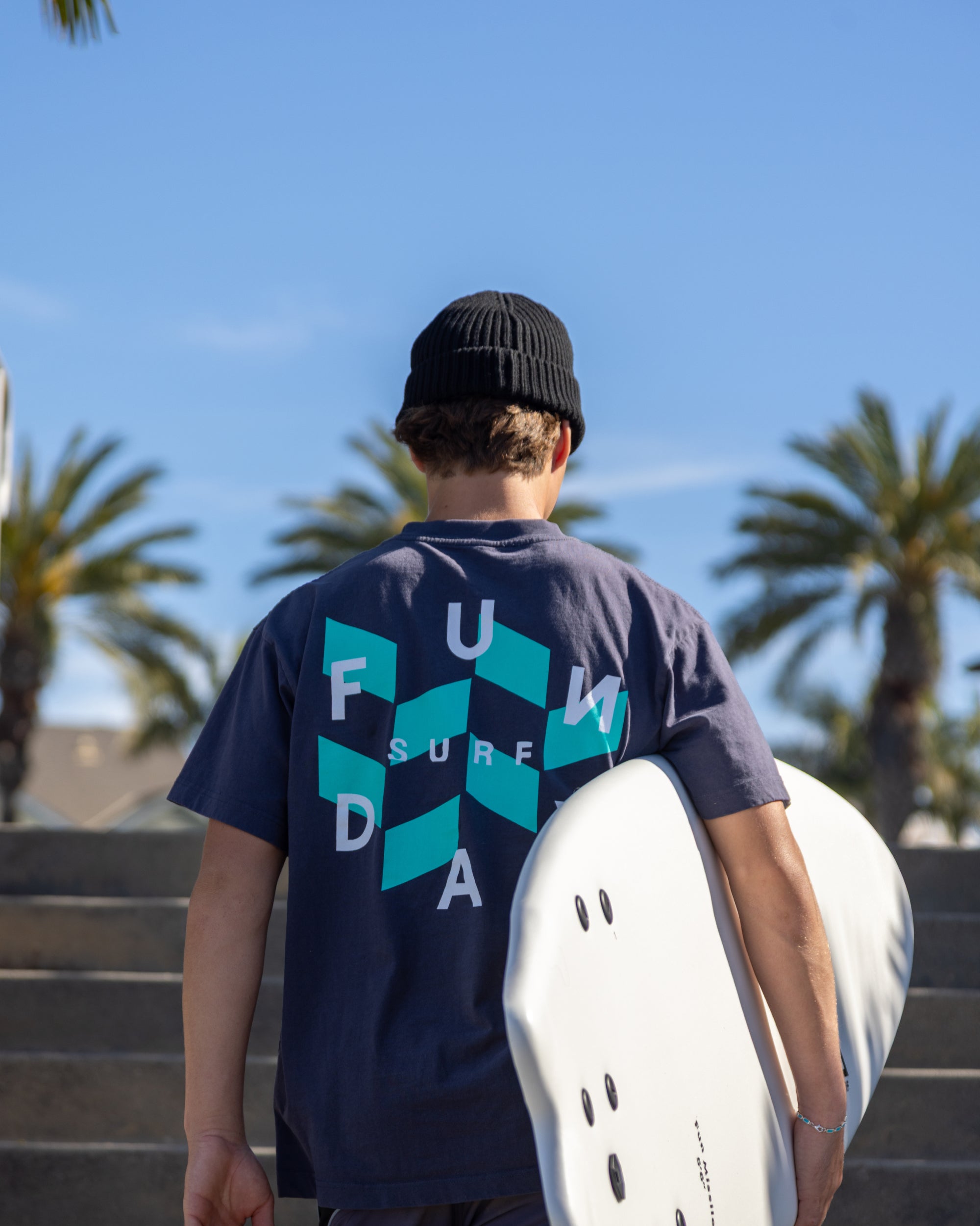 Fun Day Surf Checks Tee in Navy back graphic next to a surfboard, lifestyle view