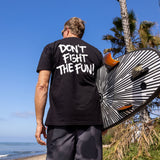 Fun Day Surf DFTF Tee in Black back graphic worn with a surfboard by the ocean, lifestyle view