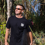 Fun Day Surf DFTF Tee in Black worn with a surfboard under the palms, lifestyle view