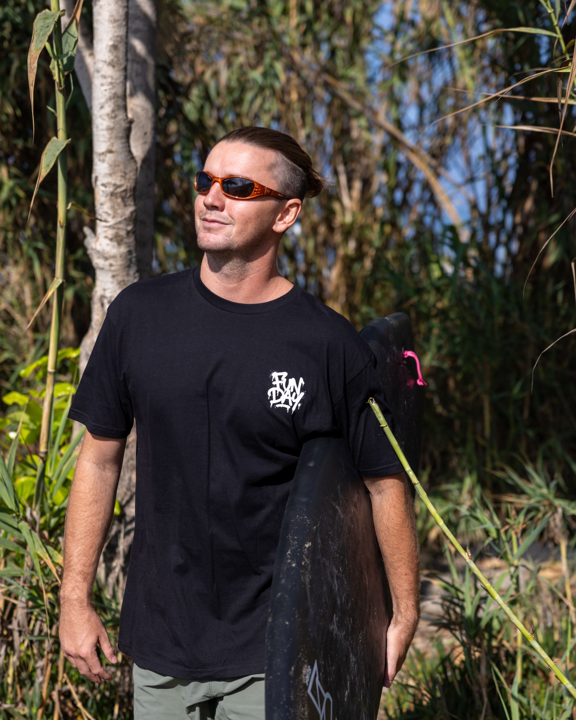 Fun Day Surf DFTF Tee in Black worn with a surfboard under the palms, lifestyle view