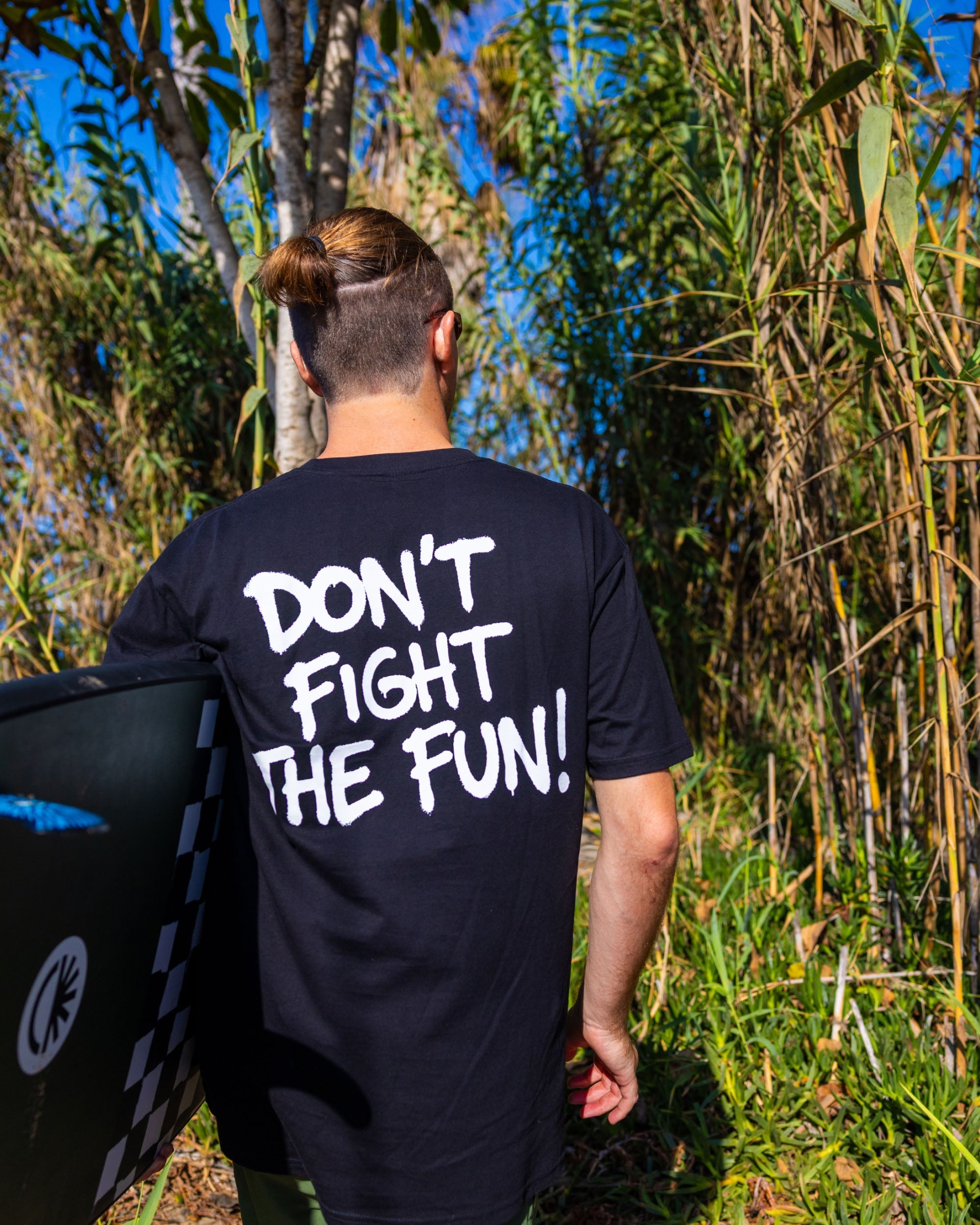 Fun Day Surf DFTF Tee in Black back graphic worn with a surfboard, lifestyle view