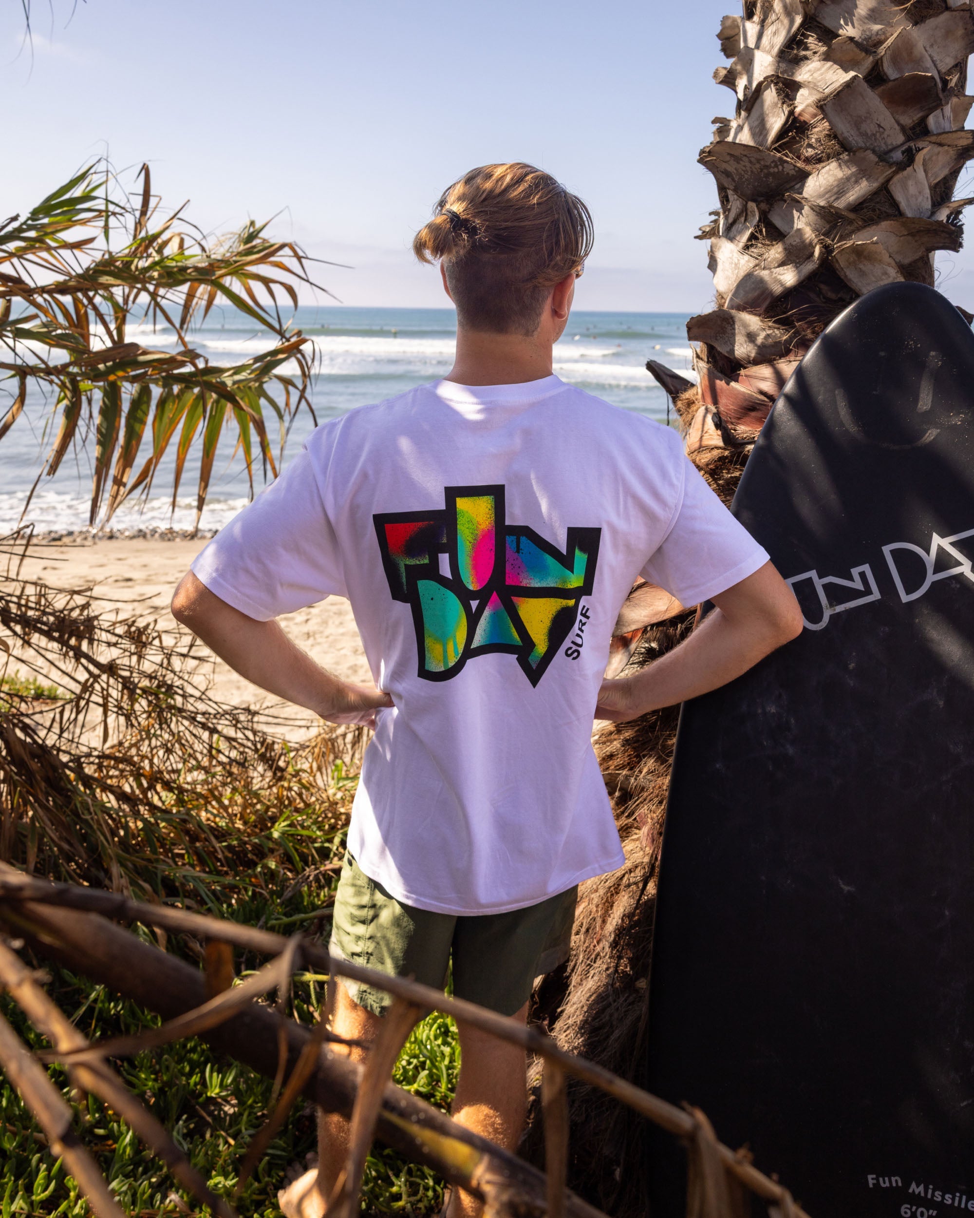 Fun Day Surf Framework Fill Tee in White back graphic worn with a surfboard, lifestyle view