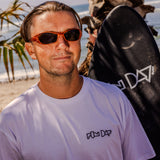 Fun Day Surf Framework Fill Tee in White worn with a surfboard at the beach, lifestyle view
