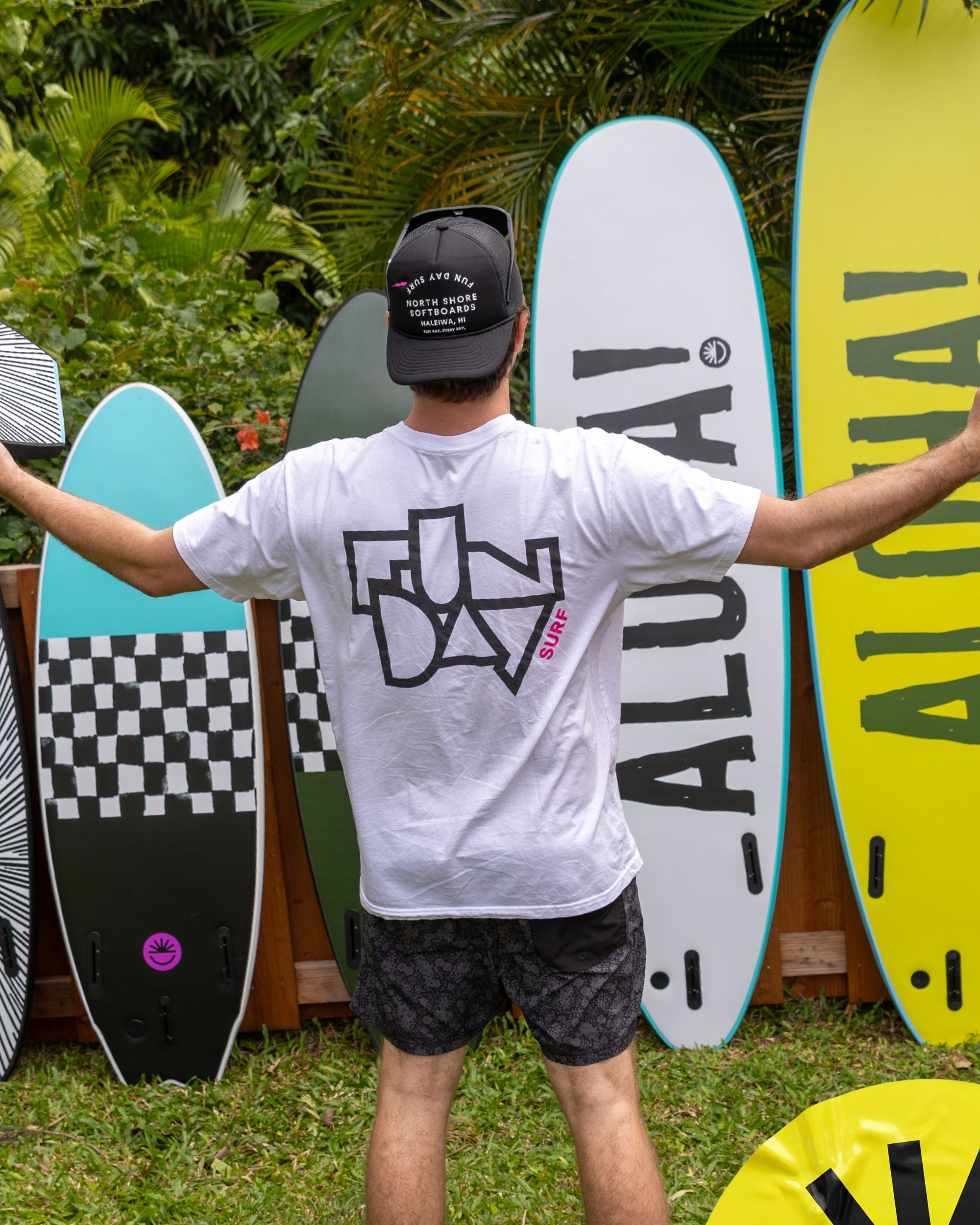 Fun Day Surf Framework Tee in White back graphic in front of surfboards, lifestyle view