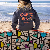 Fun Day Surf Musubi Youth Hoodie in Steel Blue back graphic worn on the beach with a surfboard, lifestyle view