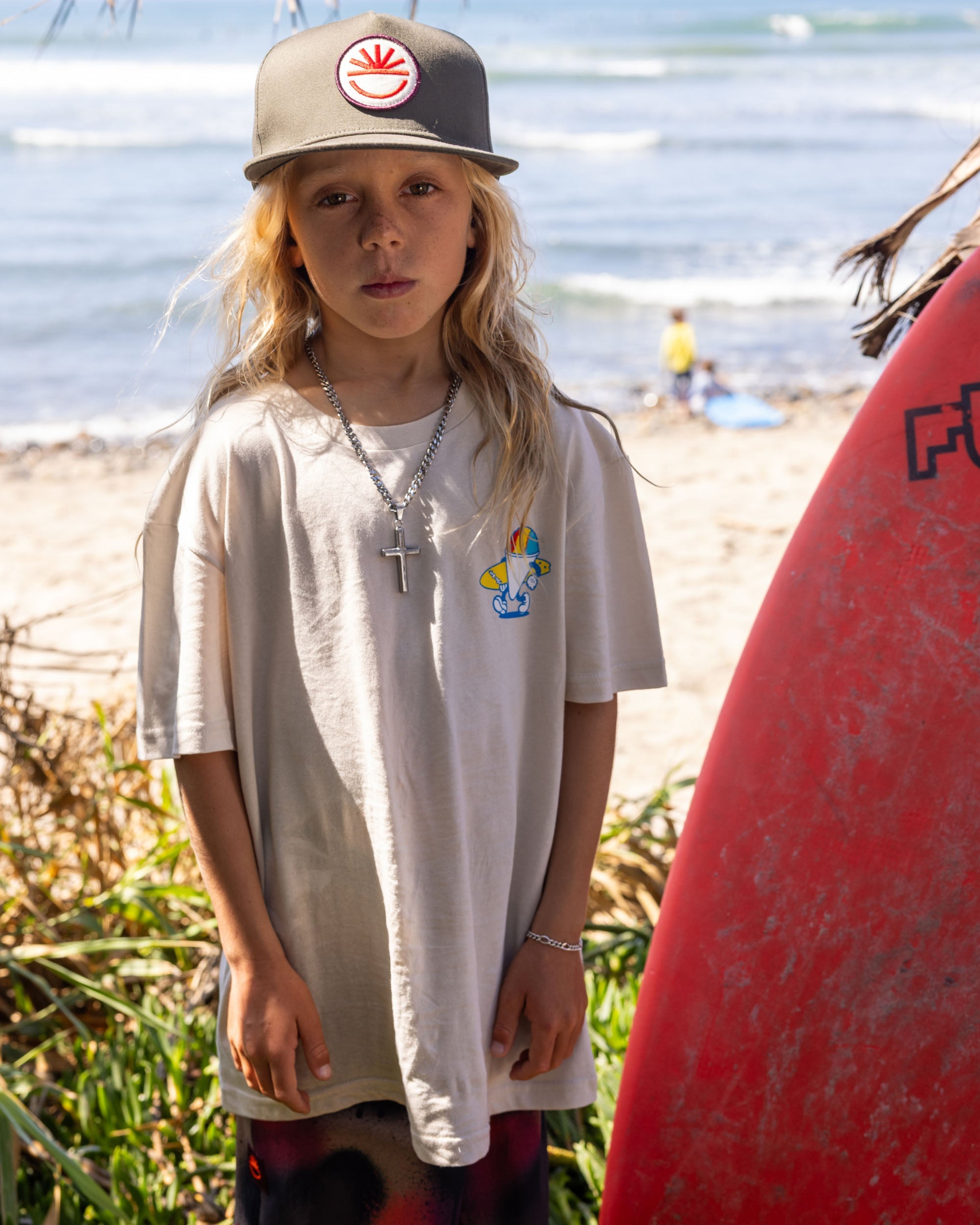 Fun Day Surf Stay Cool Youth Tee in Bone worn with a surfboard at the beach, lifestyle view